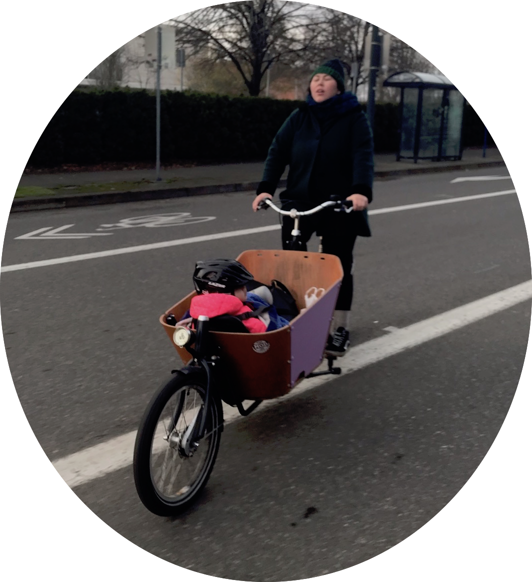 woman riding a cargo bike with a 1 year old in it.
